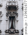 Decorative balcony and window with elaborate stucco ornamentation on historic building facade. 129692877