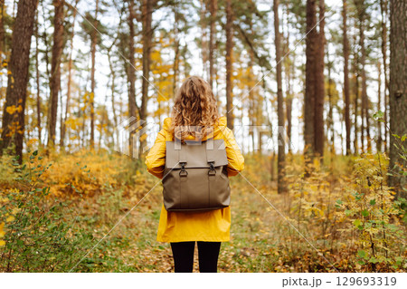 Back view. Curly woman with backpack in autumn forest enjoying nature. Concept of relaxation, nature 129693319