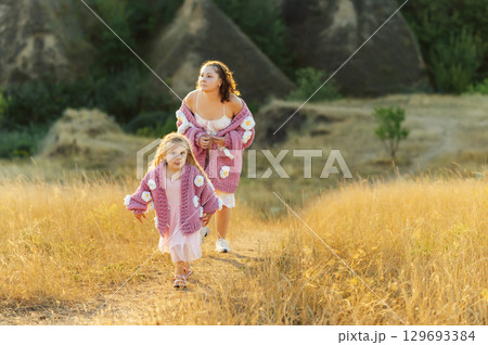 A young mother and daughter are walking in nature among the mountains in beautiful identical sweaters A young mother and daughter are walking in nature among the mountains in beautiful identical sweaters 129693384