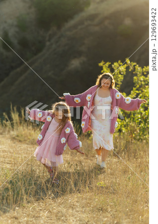 A young mother and daughter are walking in nature among the mountains in beautiful identical sweaters A young mother and daughter are walking in nature among the mountains in beautiful identical sweaters 129693422
