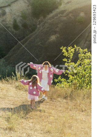 A young mother and daughter are walking in nature among the mountains in beautiful identical sweaters 129693423