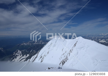 Tranquil Lake With Lush Green Forest, Snow-Capped Mountain, Blue Sky And White Clouds Tranquil Lake With Lush Green Forest, Snow-Capped Mountain, Blue Sky And White Clouds 129693808