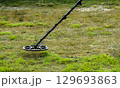 a man walks through a field with a metal detector 129693863