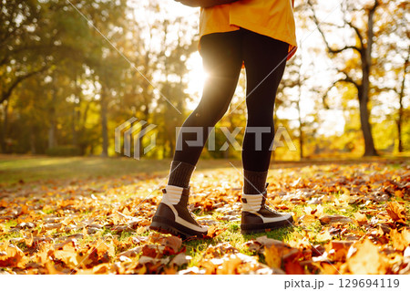 Close-up of feet in hiking boots in clearing among fallen leaves in sunny autumn park. outdoor walk. Close-up of feet in hiking boots in clearing among fallen leaves in sunny autumn park. outdoor walk. 129694119