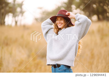 Stylish woman in sweater and hat enjoys autumn nature. People, freedom, lifestyle, travel concept. Stylish woman in sweater and hat enjoys autumn nature. People, freedom, lifestyle, travel concept. 129694441