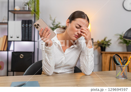 Young businesswoman frowns at smartphone sees game loss failed order budget blown client rejection 129694597