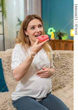 Pregnant woman bites pink donut laughs enjoys sweet treat keeps fun memory forever Pregnant woman bites pink donut laughs enjoys sweet treat keeps fun memory forever 129694661