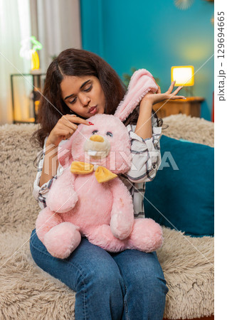 Indian woman holding pink bunny toy smiling nostalgic memory emotion missing childhood child indoors 129694665