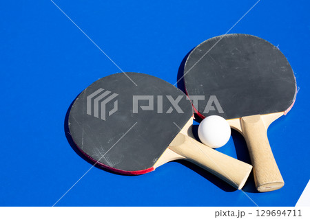 Ping pong rackets and ball on blue table. Everything you need to play table tennis. Racket sport for active recreation. Background photo for ad for ping pong section 129694711