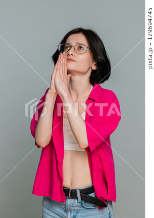 Woman looking upwards holding hands in prayer gesture asking God for help emotional hopeful plea 129694745