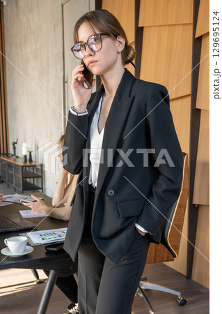 Businesswoman in office workspace, female professional at work, talking on phone during communication with colleagues in meeting and discussion. 129695124