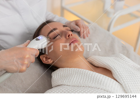 Woman gets RF lifting therapy under eyes with modern device in beauty cosmetology clinic session 129695144