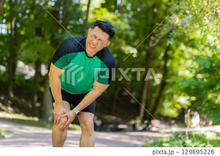 Japanese runner athlete man with muscle pain in park trauma injury while jogging leg muscle cramp Japanese runner athlete man with muscle pain in park trauma injury while jogging leg muscle cramp 129695226