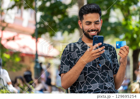 Indian man using credit bank card smartphone transferring money purchases online shopping outdoors 129695254