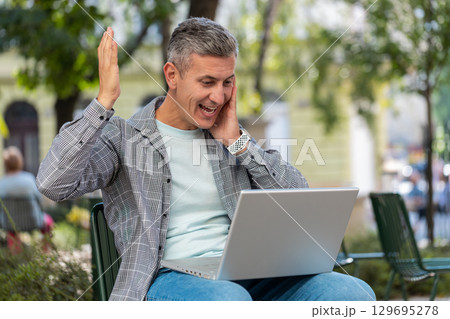 Happy man freelancer working on laptop screams in triumph win celebrating success sitting on chair 129695278