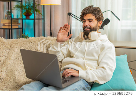 Confident young man on sofa couch using laptop making an online video conference call at distance 129695279