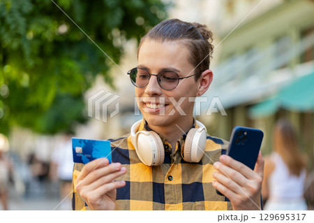 Man using credit bank card smartphone while transferring money, purchases online shopping outdoors Man using credit bank card smartphone while transferring money, purchases online shopping outdoors 129695317