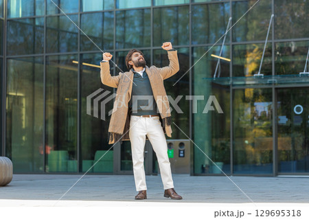 Excited man looking surprised clenching fists, shocked by sudden victory standing on city street 129695318