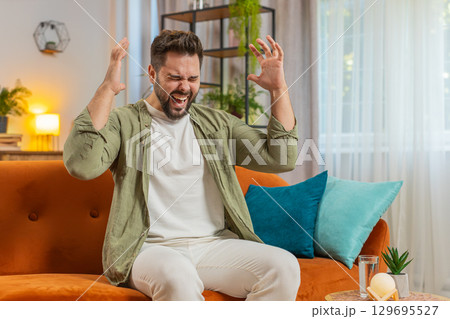 Sad young man feeling loneliness, nervous breakdown, crying shouting on sofa in living room at home 129695527