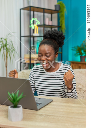 African American woman celebrating good news online email laptop screen happy victory win indoors 129695565