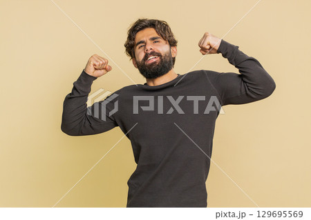Fit sporty man showing biceps and looking confident, feeling power strength on beige background 129695569