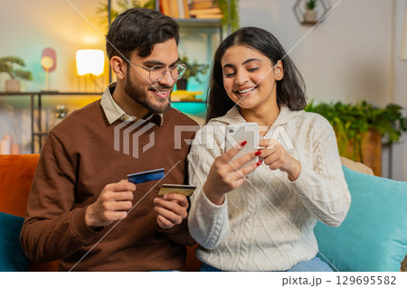 Happy young couple together doing online shopping by entering credit card number on smartphone 129695582