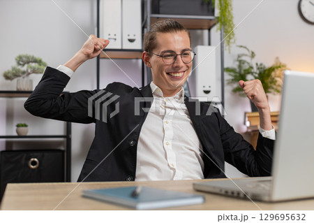 Stylish young Caucasian manager in suit working on laptop netbook shocked by sudden victory at home Stylish young Caucasian manager in suit working on laptop netbook shocked by sudden victory at home 129695632