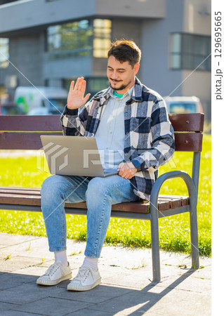 Mature businessman on video call using laptop while sitting on bench in downtown city street 129695665