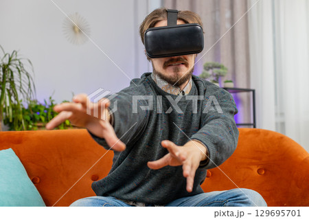 Excited man use virtual reality futuristic technology headset play simulation 3D video game at home 129695701