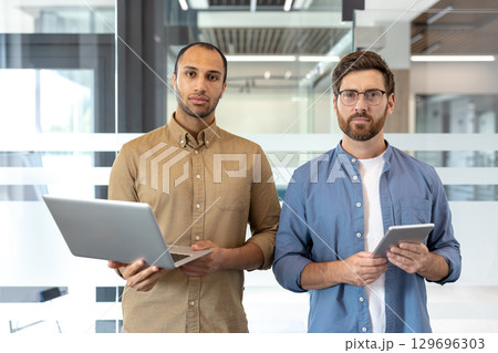 Dynamic collaboration of two professionals standing in a modern office, showcasing teamwork and technology use in a business environment. 129696303