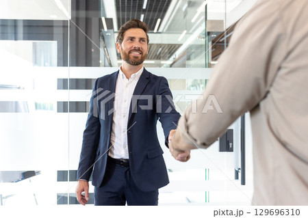 Professional meeting with a handshake between a confident businessman and a colleague in a modern workspace, symbolizing cooperation, teamwork, and new opportunities for successful partnerships. 129696310