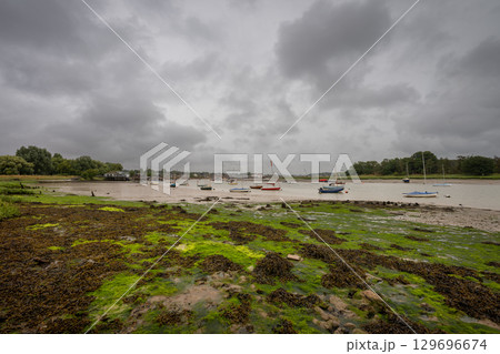 River Deben at low tide with small boats under a stormy sky. View towards the historic town of Woodbridge in Suffolk, UK. River Deben at low tide with small boats under a stormy sky. View towards the historic town of Woodbridge in Suffolk, UK. 129696674