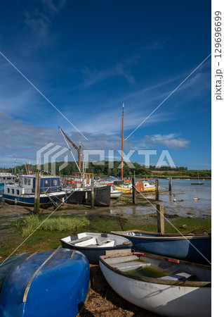 Small boats on a sunny day. View of the quay at low tide on the River Deben in the historic town of Woodbridge in Suffolk, UK. 129696699