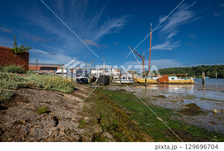 Boats on a sunny day at the quay in the historic town of Woodbridge in Suffolk, UK. View at low tide on the River Deben. Boats on a sunny day at the quay in the historic town of Woodbridge in Suffolk, UK. View at low tide on the River Deben. 129696704