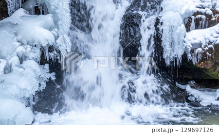 Frozen Waterfall with Ice and Snow in Winter Landscape and Mountain Backdrop 129697126