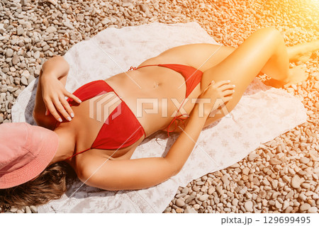 Woman Sunbathing Beach Summer - A woman in a red bikini sunbathes on a beach towel, basking in the summer sun. Woman Sunbathing Beach Summer - A woman in a red bikini sunbathes on a beach towel, basking in the summer sun. 129699495