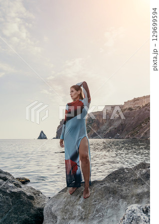 Woman Dress Ocean Rock Beach - A woman in a long dress standing on a rock by the ocean at sunset. 129699594