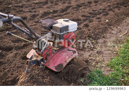 Garden tiller machine working on soil in sunny outdoor setting for farming 129699963