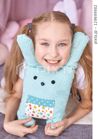 Smiling caucasian young girl with pigtails holding a cute gingham plush toy Smiling caucasian young girl with pigtails holding a cute gingham plush toy 129699982