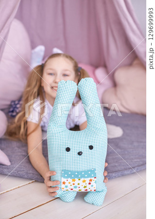 Young caucasian girl playing in cozy tent with stuffed bunny toy in playroom 129699993