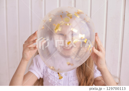 Caucasian female child enjoying balloon fun with golden confetti in white room Caucasian female child enjoying balloon fun with golden confetti in white room 129700113