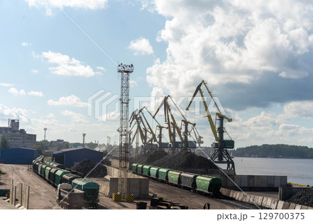 Industrial port with cranes, trains, and large piles of coal, illustrating a logistics and cargo hub Industrial port with cranes, trains, and large piles of coal, illustrating a logistics and cargo hub 129700375