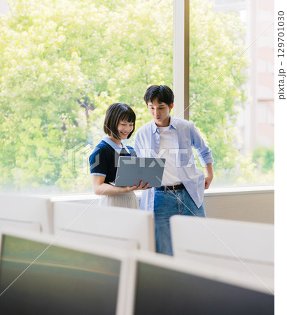 　窓際で会話する大学生男女とノートPC 129701030
