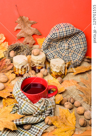 Fall season to do list concept. Mug cozy aromatic tea beverage in scarf and treats. Mug of tea surrounded by scarf red background with fallen maple leaves and walnuts. Cozy autumnal atmosphere 129701555