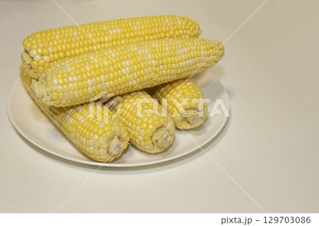 Raw cobs of sweet corn on plate against background. Tasty sweet corn on cobs 129703086