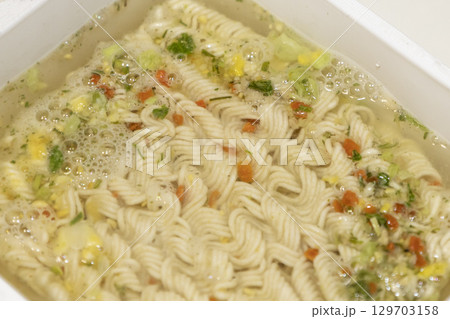 Instant noodles with spices and water on white plastic box. 129703158