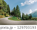 Summer mountain landscape with a winding asphalt road. View from a curve, surrounded by green trees and blue sky. 129703193