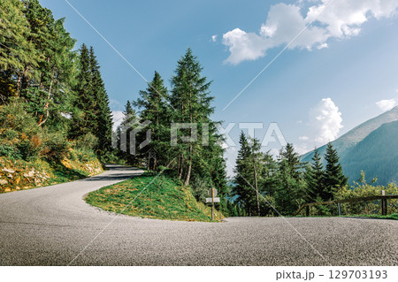 Summer mountain landscape with a winding asphalt road. View from a curve, surrounded by green trees and blue sky. Summer mountain landscape with a winding asphalt road. View from a curve, surrounded by green trees and blue sky. 129703193
