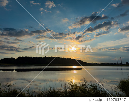 Sunset over a tranquil lake reflecting clouds and trees in the evening sky near a natural landscape Sunset over a tranquil lake reflecting clouds and trees in the evening sky near a natural landscape 129703747