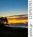 Spectacular sunset over the tranquil beach with silhouetted trees and gentle waves at dusk 129703765